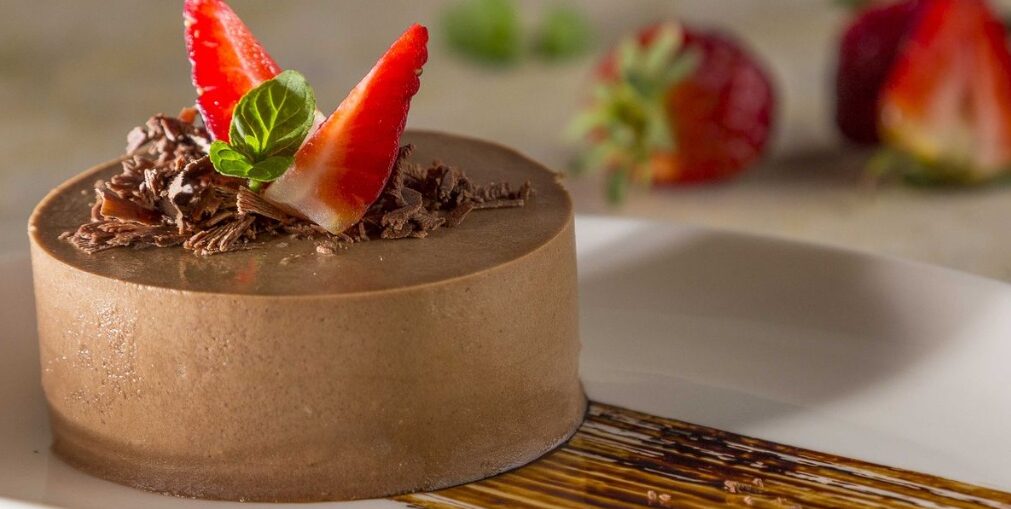 Bột Whipping Cream Dùng Làm Mousse Được Không? Cách Sử Dụng Và Lưu Ý 5 Bánh mousse chocolate đúc khuôn tròn mịn màng rắc vụn socola trang trí dâu tây tươi và lá bạc hà trên đĩa sứ trắng