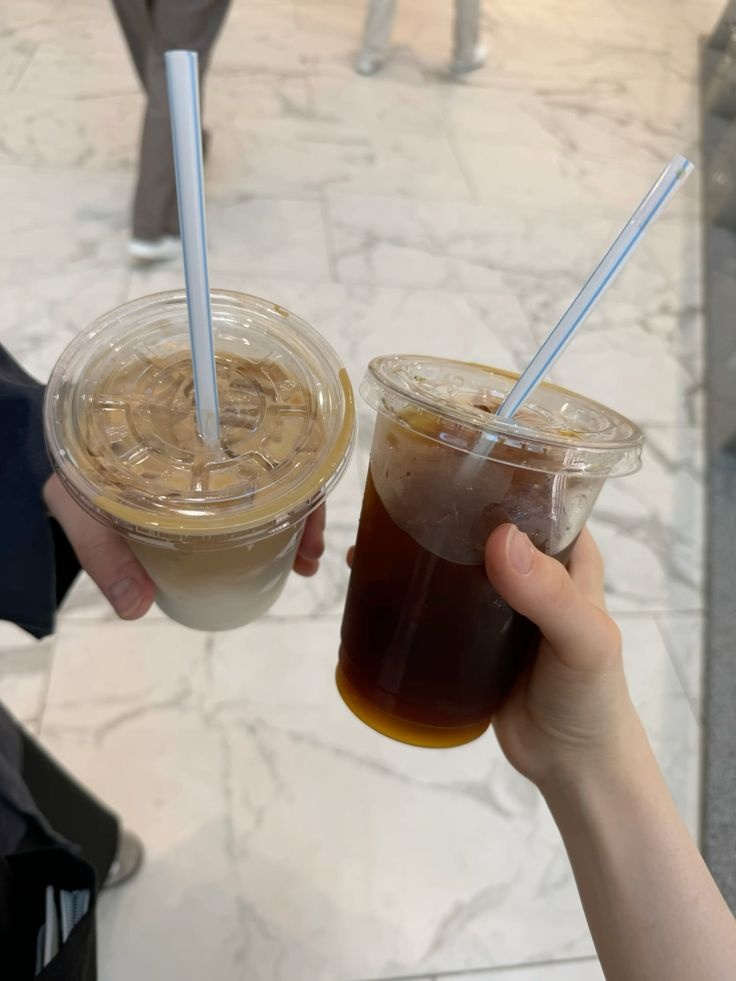Trend Đồ Uống Cho Gen Z: Quán F&B Nên Theo Điều Gì, Bỏ Điều Gì? 5 Hai tay cầm ly cà phê latte phân tầng và ly americano đá mang đi bằng ly nhựa trong suốt có ống hút