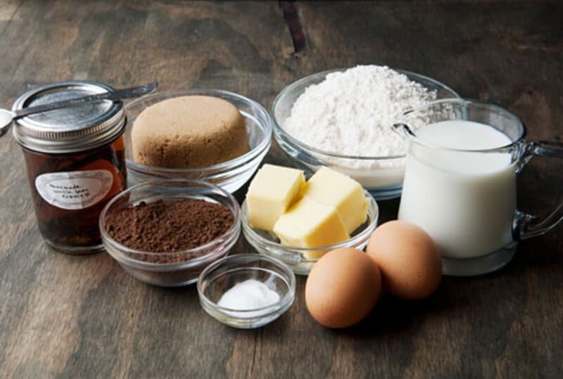 Nguyên Liệu Làm Bánh Cơ Bản Gồm Những Gì? Công Dụng Và Cách Lựa Chọn 7 Bàn gỗ bày các bát nguyên liệu làm bánh chocolate gồm bơ lạt cắt khối bột cacao đường nâu bột mì trứng gà và sữa tươi