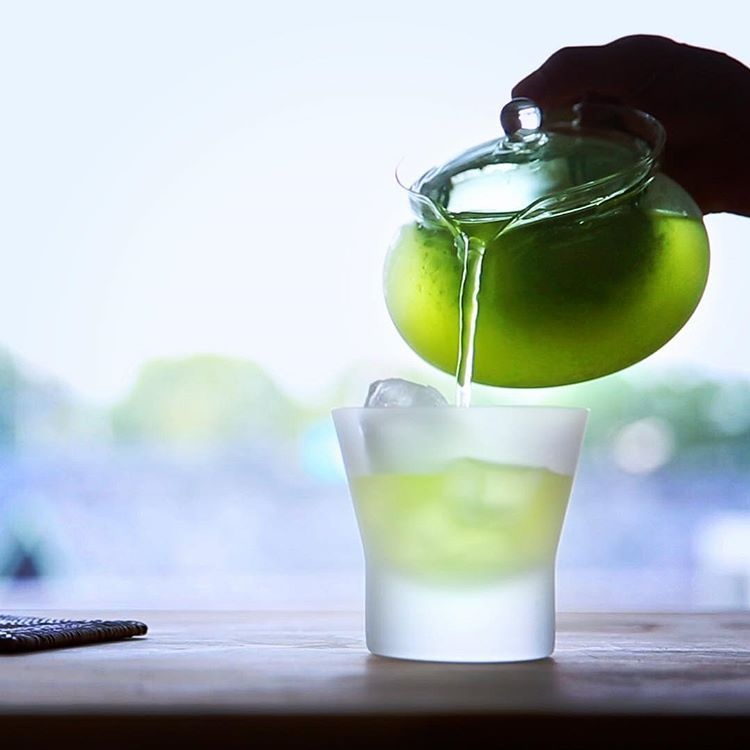 Cold Brew Tea Là Gì? Có Phù Hợp Với Menu Quán F&B Không? 4 Rót trà xanh ủ lạnh Cold Brew màu xanh ngọc bích từ bình thủy tinh vào ly đá mờ