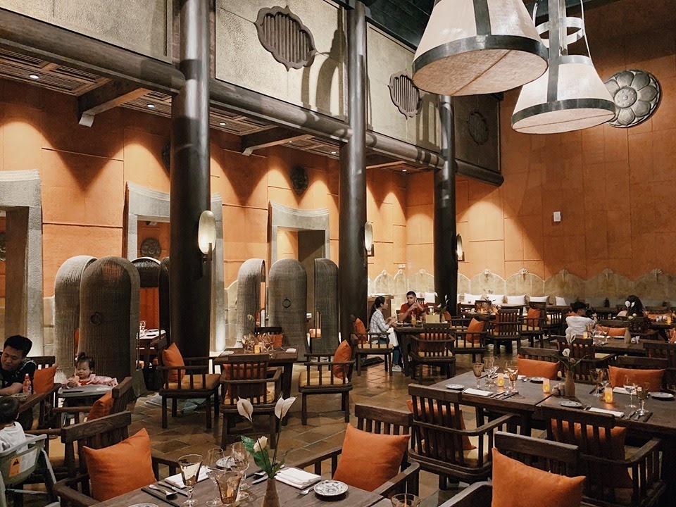 Kiến Thức Kinh Doanh F&B Cho Người Mới: Hướng Dẫn Từ A–Z 4 Không gian nội thất nhà hàng cao cấp phong cách Á Đông đương đại với cột gỗ trần cao đèn thả chao nón và bàn ăn gỗ đệm cam sang trọng