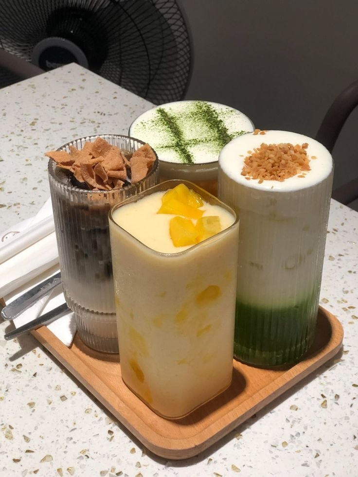 Menu Tết 2027: Những Ý Tưởng Đồ Uống Và Dessert Dễ Ứng Dụng 6 Khay gỗ đựng 4 ly đồ uống hiện đại gồm matcha latte kem béo, cà phê dừa nướng, sinh tố xoài và trà foam tuyết